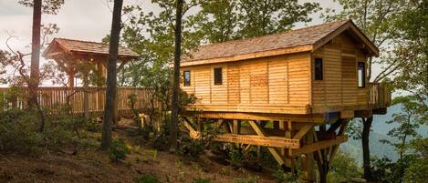 Una casa en el árbol de madera con balcón, rodeada de árboles y un paisaje natural.