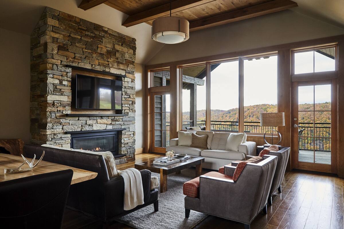 A spacious living room with a stone fireplace, a large TV, and a view of the outdoors.