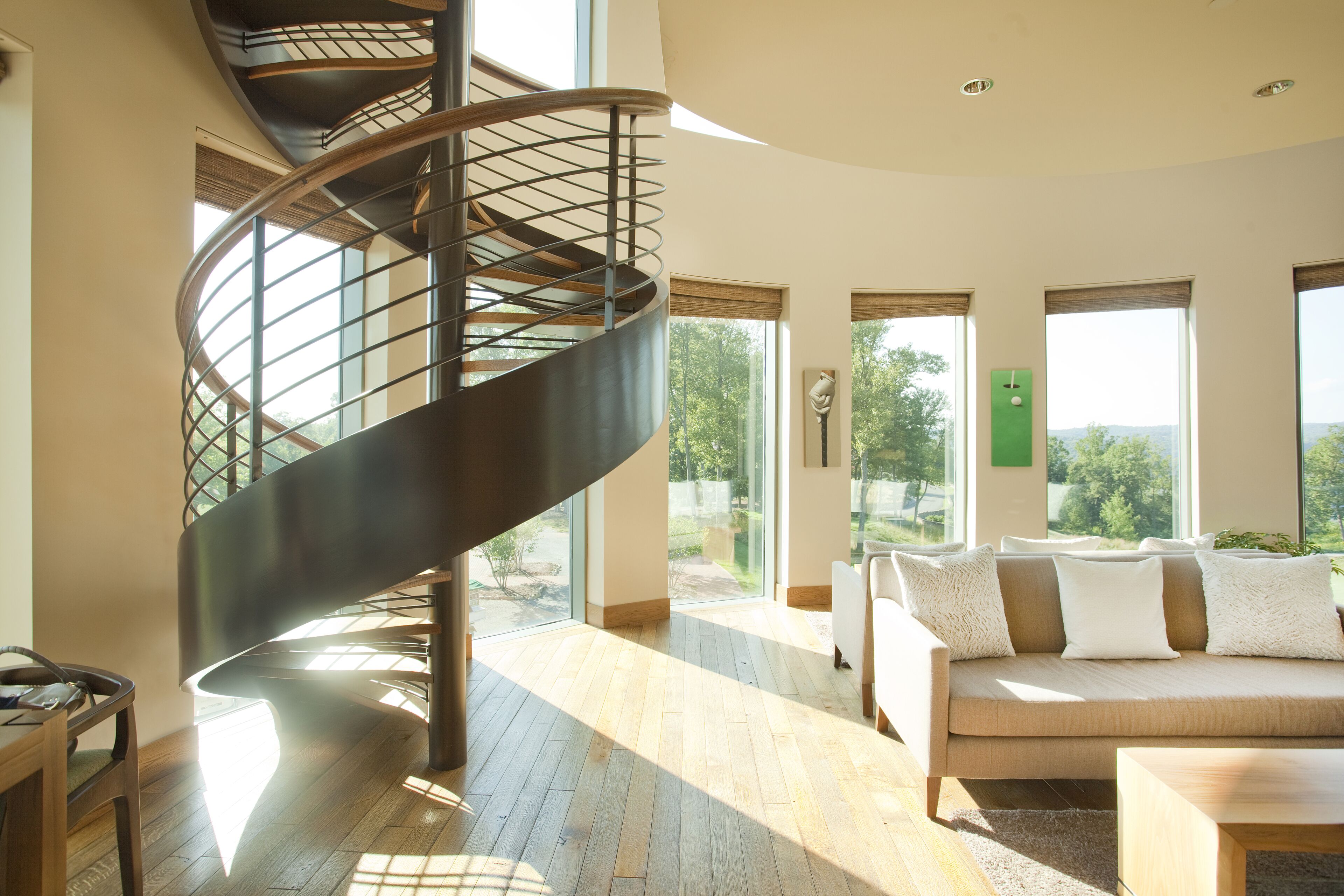 Un interior moderno con una escalera en espiral, un conjunto de sofás y ventanas amplias que ofrecen vistas al exterior.