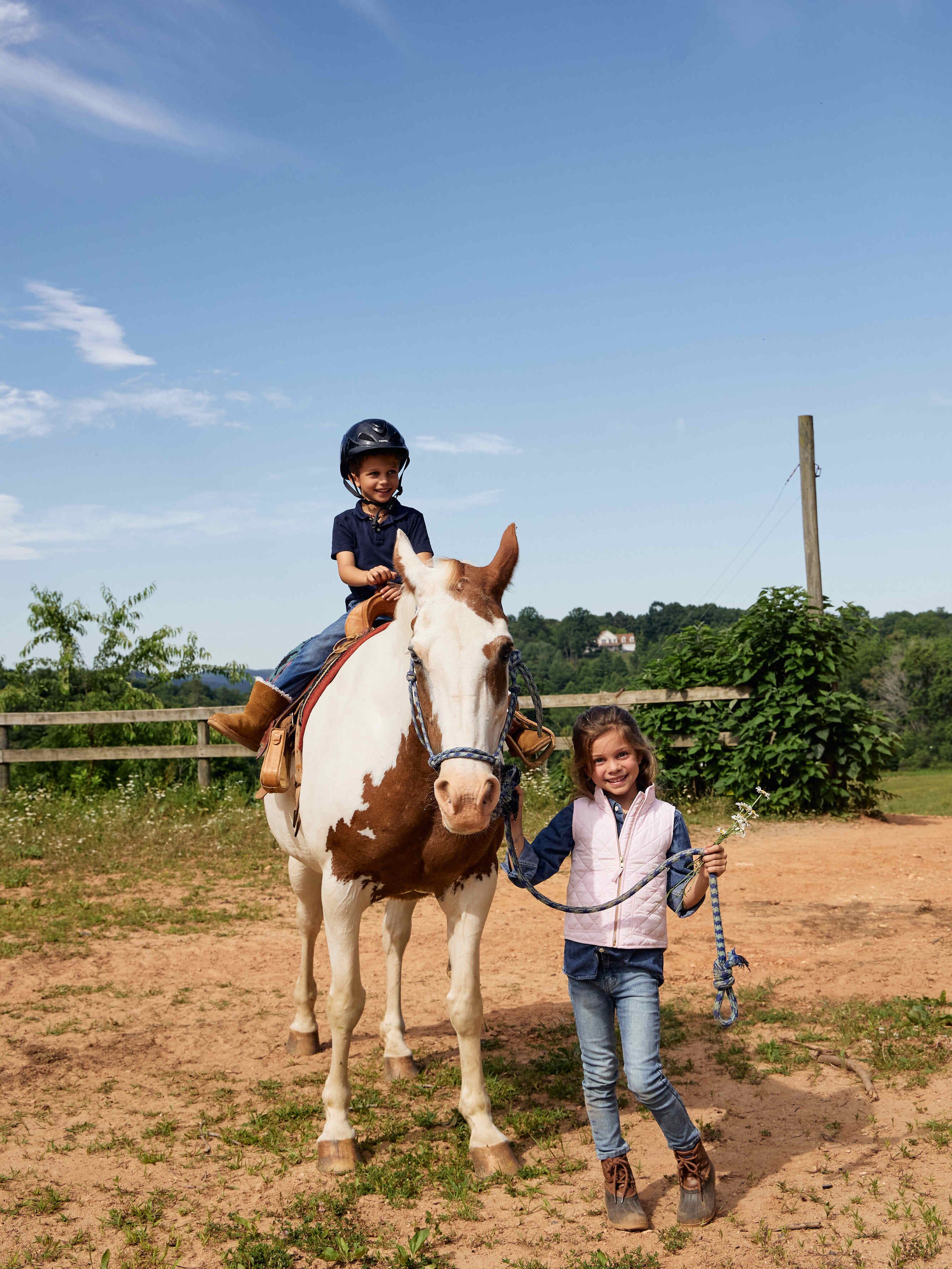 A child on a horse in a fenced outdoor area with greenery in the background.