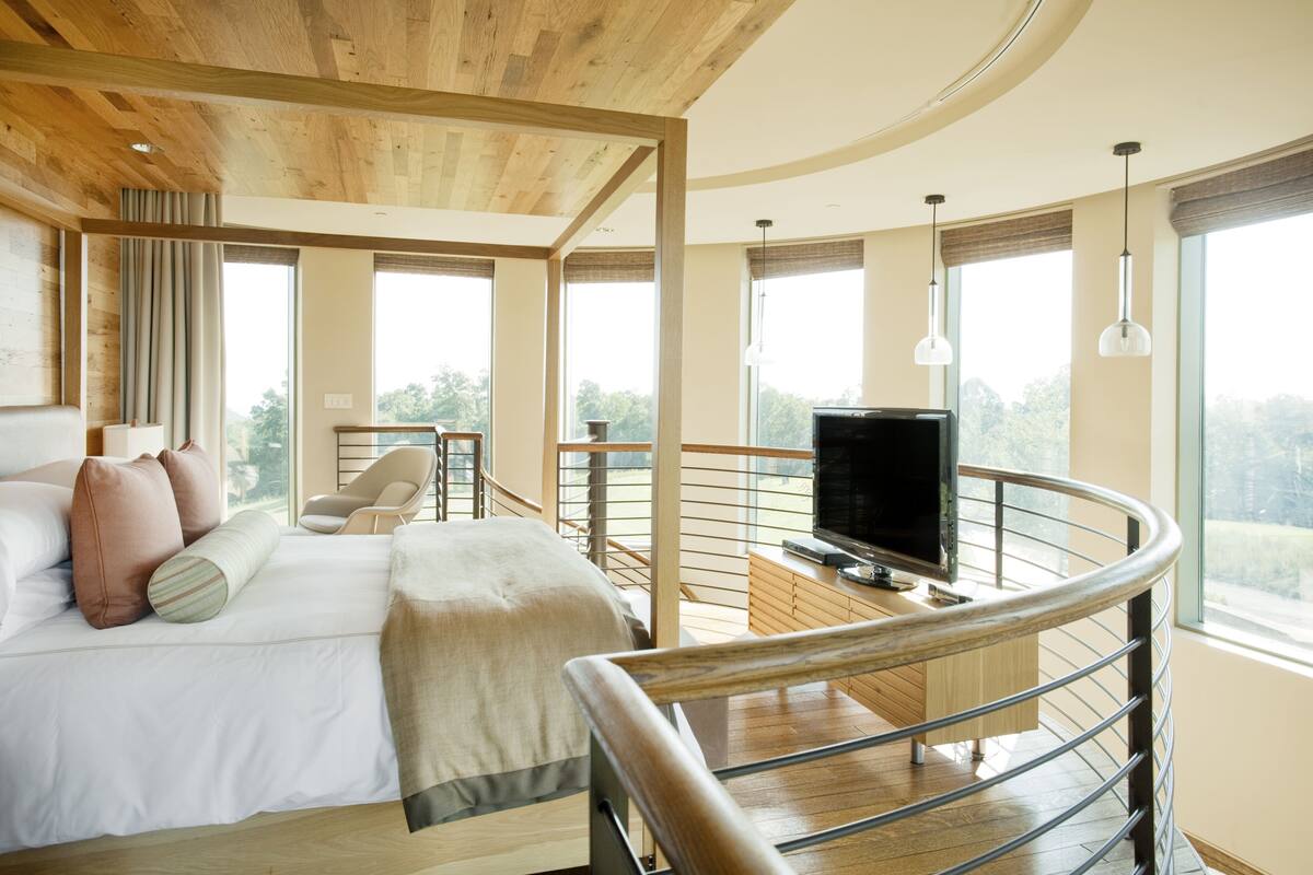 A bedroom with a large bed, a TV, and a balcony with a railing.
