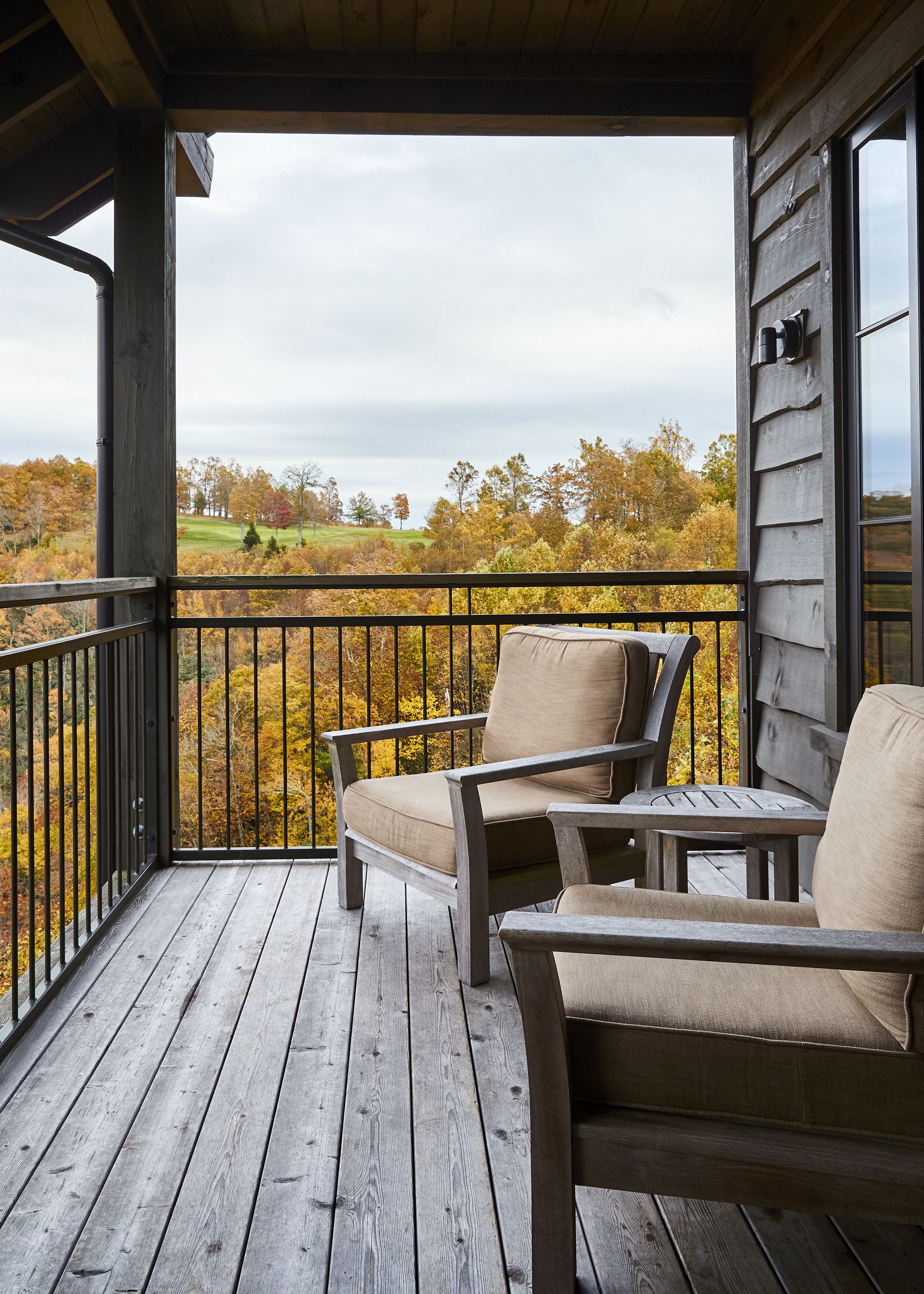 A wooden deck with two chairs and a table, overlooking a landscape with autumn foliage.