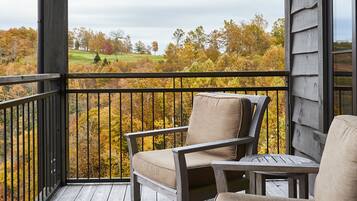 A wooden deck with two chairs and a table, overlooking a landscape with autumn foliage.