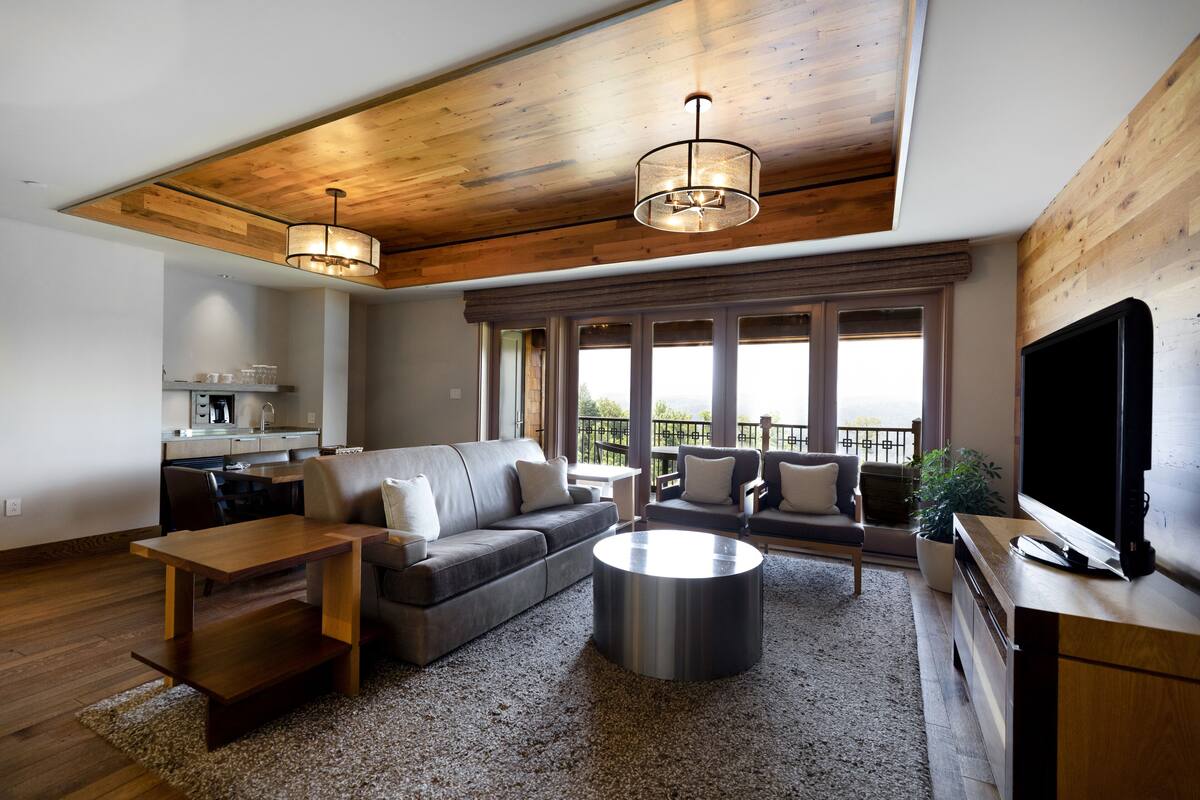 A modern living room with a wooden ceiling, a large window, a sofa, a coffee table, and a TV.