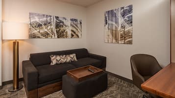 A modern hotel room with a dark grey sofa, a wooden coffee table, a single armchair, and two abstract paintings on the walls.