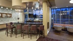 A modern bar area with a bar counter, stools, and a seating area with round tables and chairs. - SpringHill Suites Philadelphia Airport Ridley Park (Ridley Park)