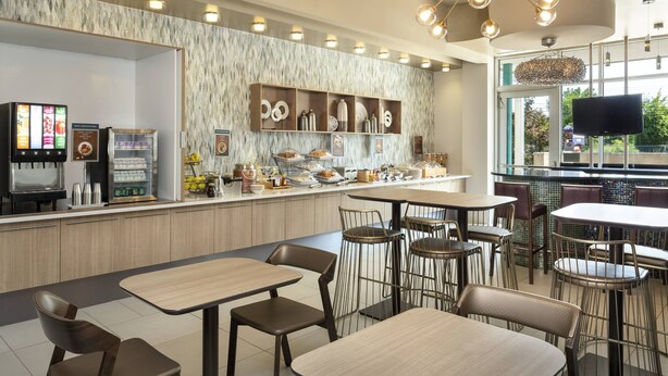 A modern cafe with a marble wall, a coffee machine, and a variety of food items on display. - SpringHill Suites Philadelphia Airport Ridley Park (Ridley Park)