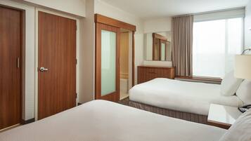 Una habitación de hotel con dos camas, un baño, un ventanal grande con cortinas y un espejo.