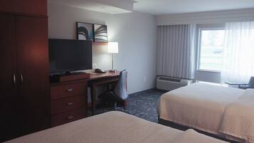 A hotel room with two beds, a desk with a television, a chair, and a window with curtains.