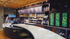 A bar area with a curved counter, bar stools, a menu board, shelves with bottles, and a television. - Courtyard by Marriott Owensboro (Owensboro)