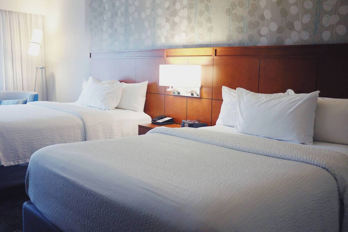 Una habitación de hotel con dos camas, una mesita de noche con lámpara y un papel tapiz estampado.