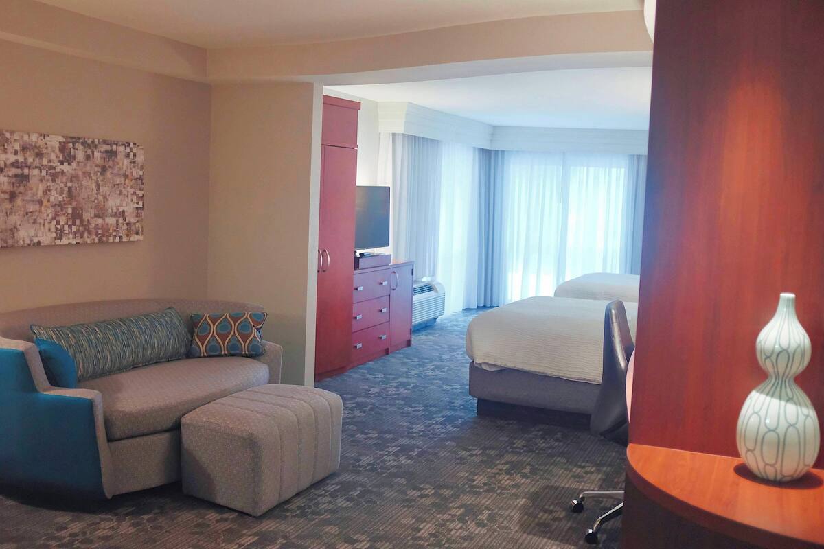 Habitación de hotel con sofá, reposapiés, cama, televisor y un florero decorativo.