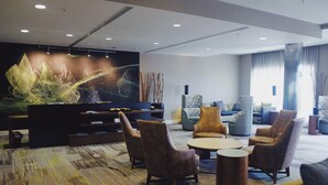 A modern lounge area with a large abstract painting, comfortable seating, and a patterned carpet. - Courtyard by Marriott Owensboro (Owensboro)