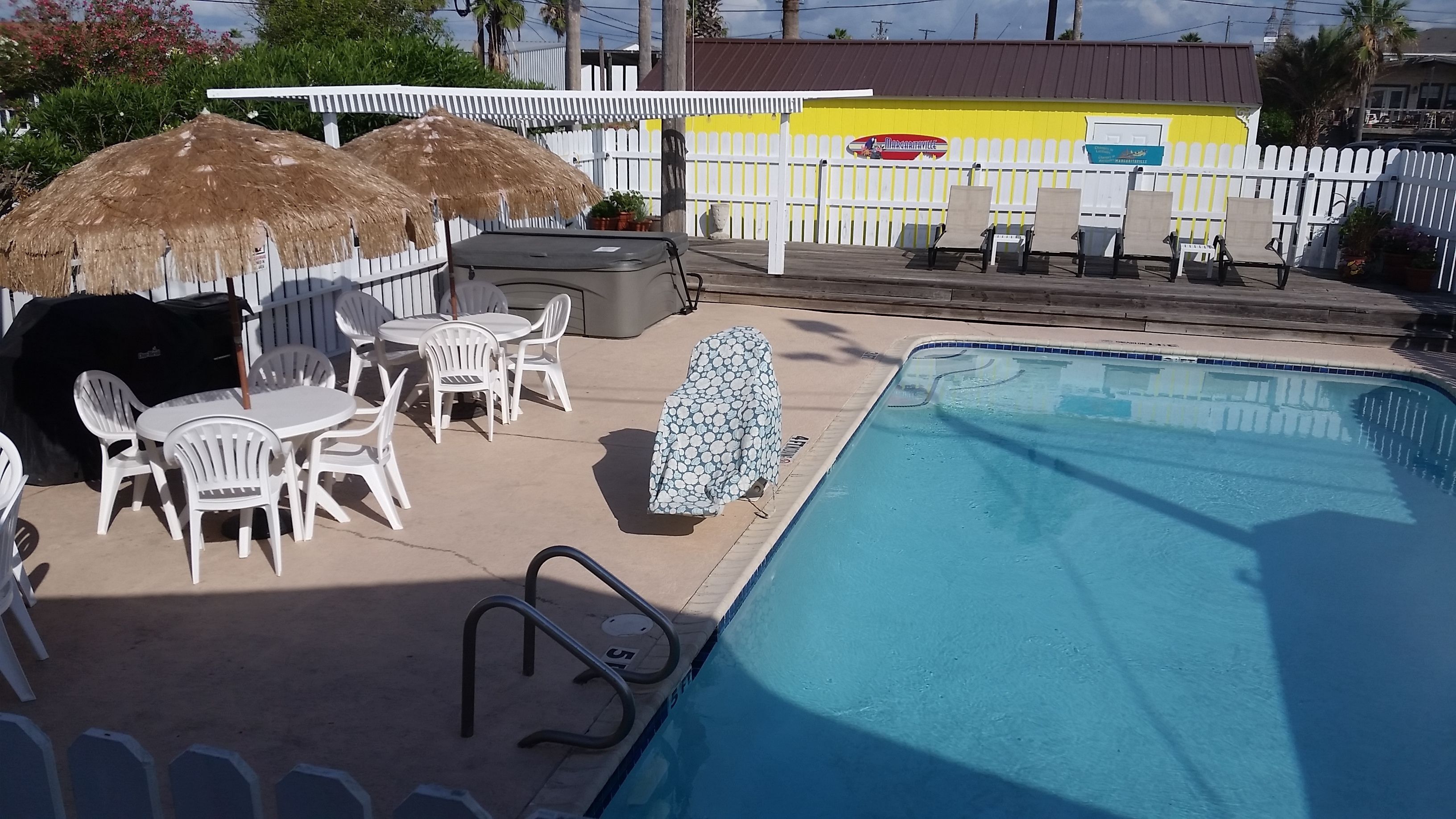 A pool area with a white fence, lounge chairs, and a barbecue grill.