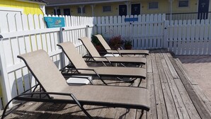 Een terras met vier lounge fauteuils, een wit hek en een gebouw met genummerde deuren op de achtergrond.