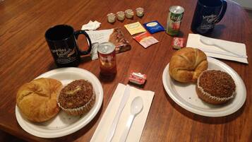 A table with food items, a coffee mug, a can of soda, and a croissant.