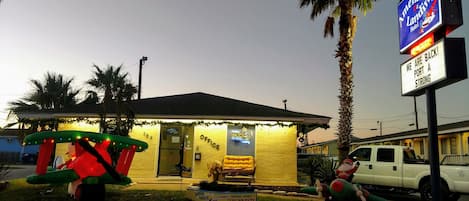 Un hotel con una pequeña zona de estar al aire libre, un cartel y un vehículo estacionado.