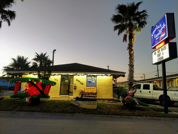 Un hotel con una pequeña zona de estar al aire libre, un cartel y un vehículo estacionado.