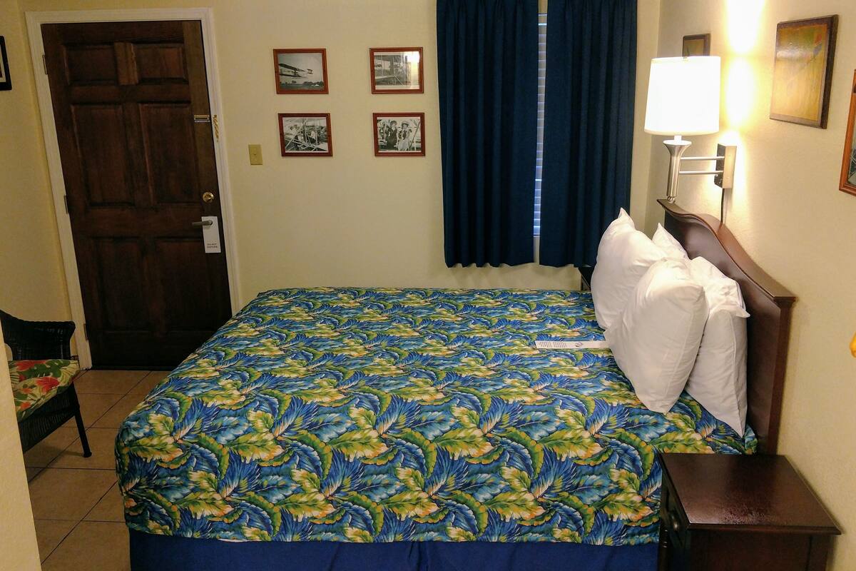 Une chambre d’hôtel avec un lit, une table de chevet, une lampe, une porte et des tableaux encadrés au mur.