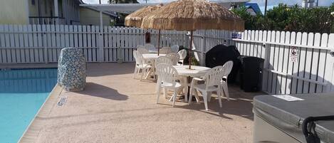 A poolside area with a covered table and chairs, a barbecue grill, and a fenced pool.