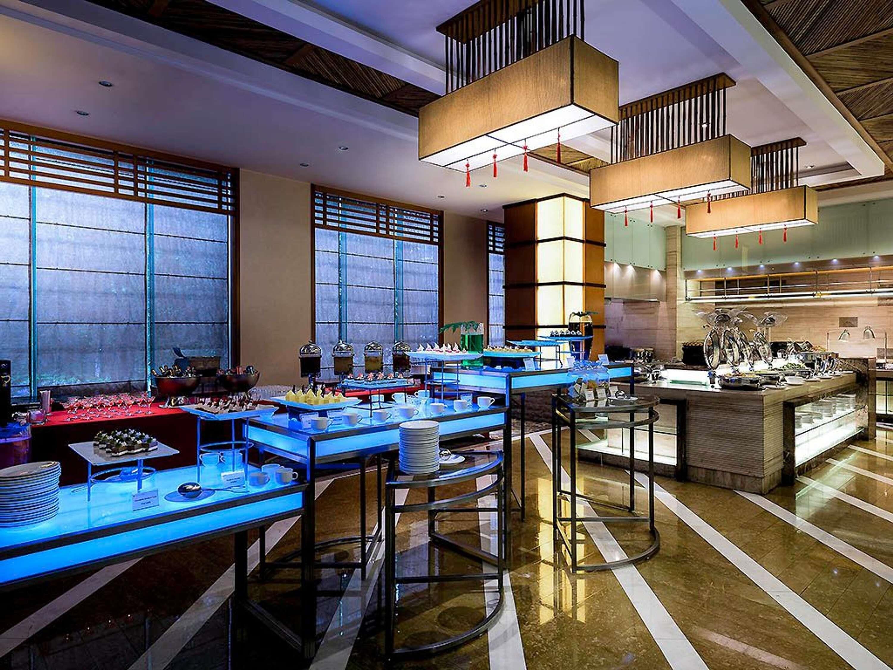 A modern hotel lobby with a buffet setup, large windows, and contemporary lighting fixtures.