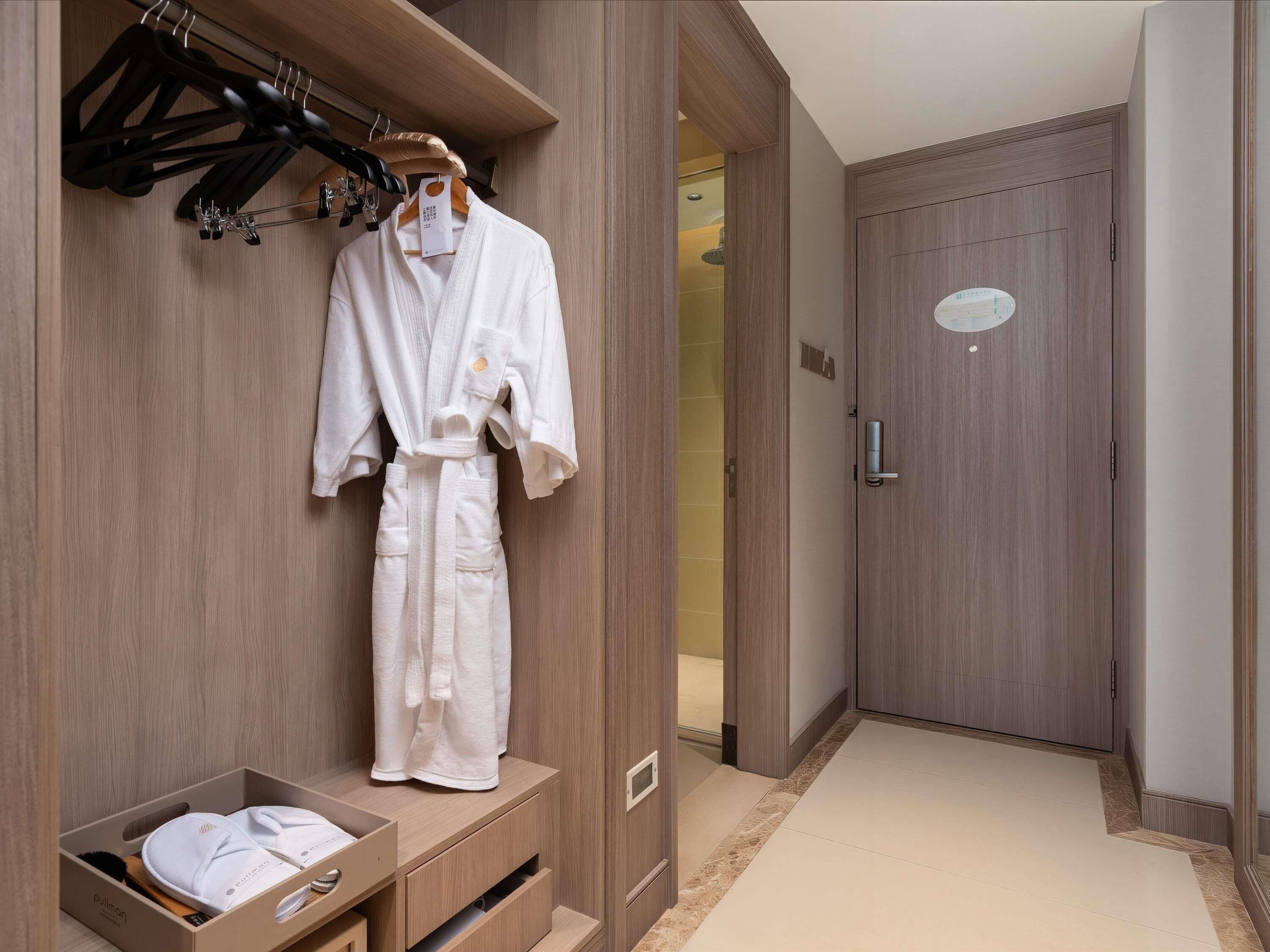 A hotel room with a wooden wardrobe, a robe hanging on a rack, and a small storage box with towels.