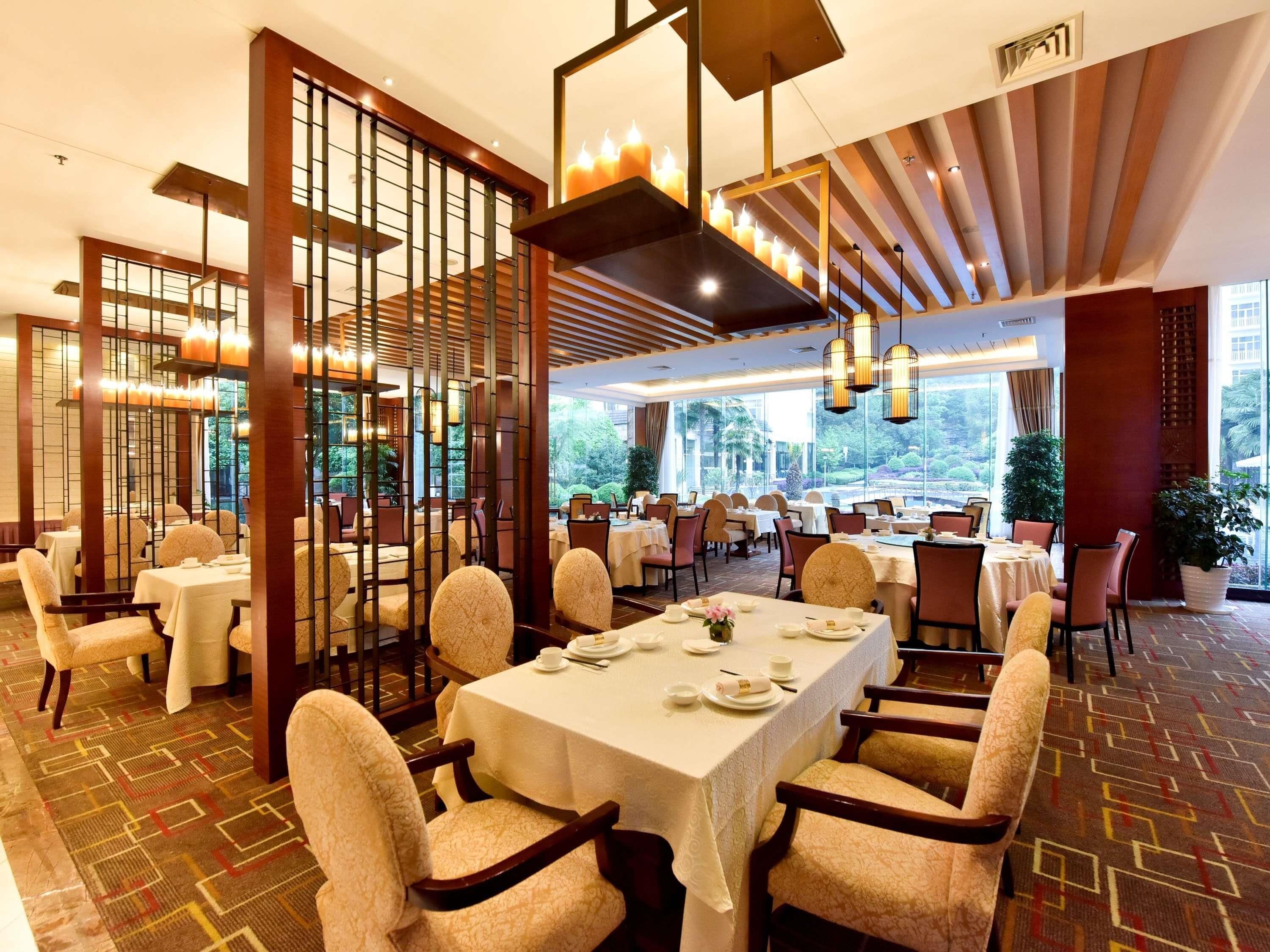 Un restaurant où les tables sont dressées pour le service, avec une vue sur la verdure et un décor intérieur moderne.