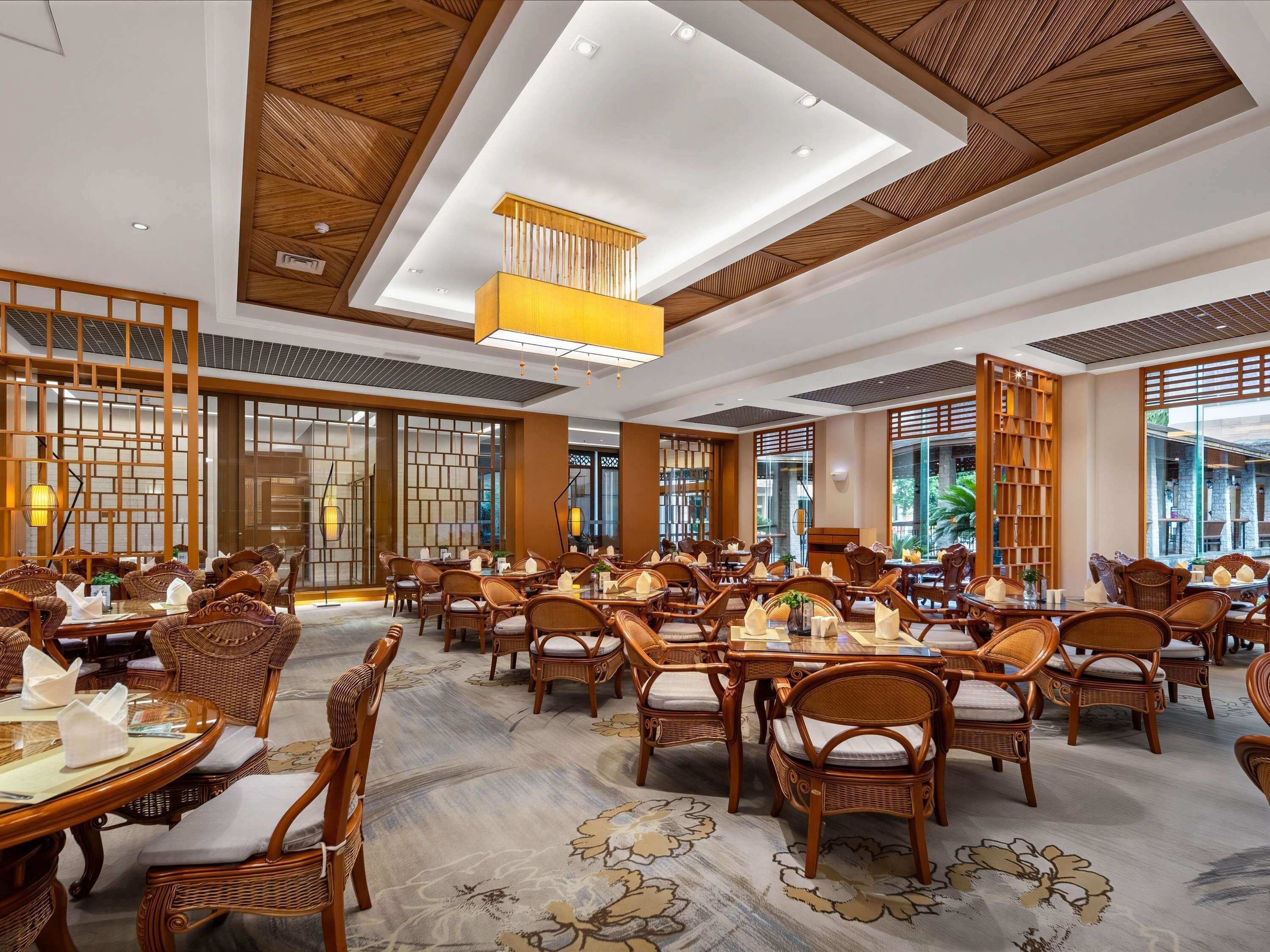 A spacious dining area with multiple tables and chairs, wooden ceiling beams, and large windows allowing natural light.