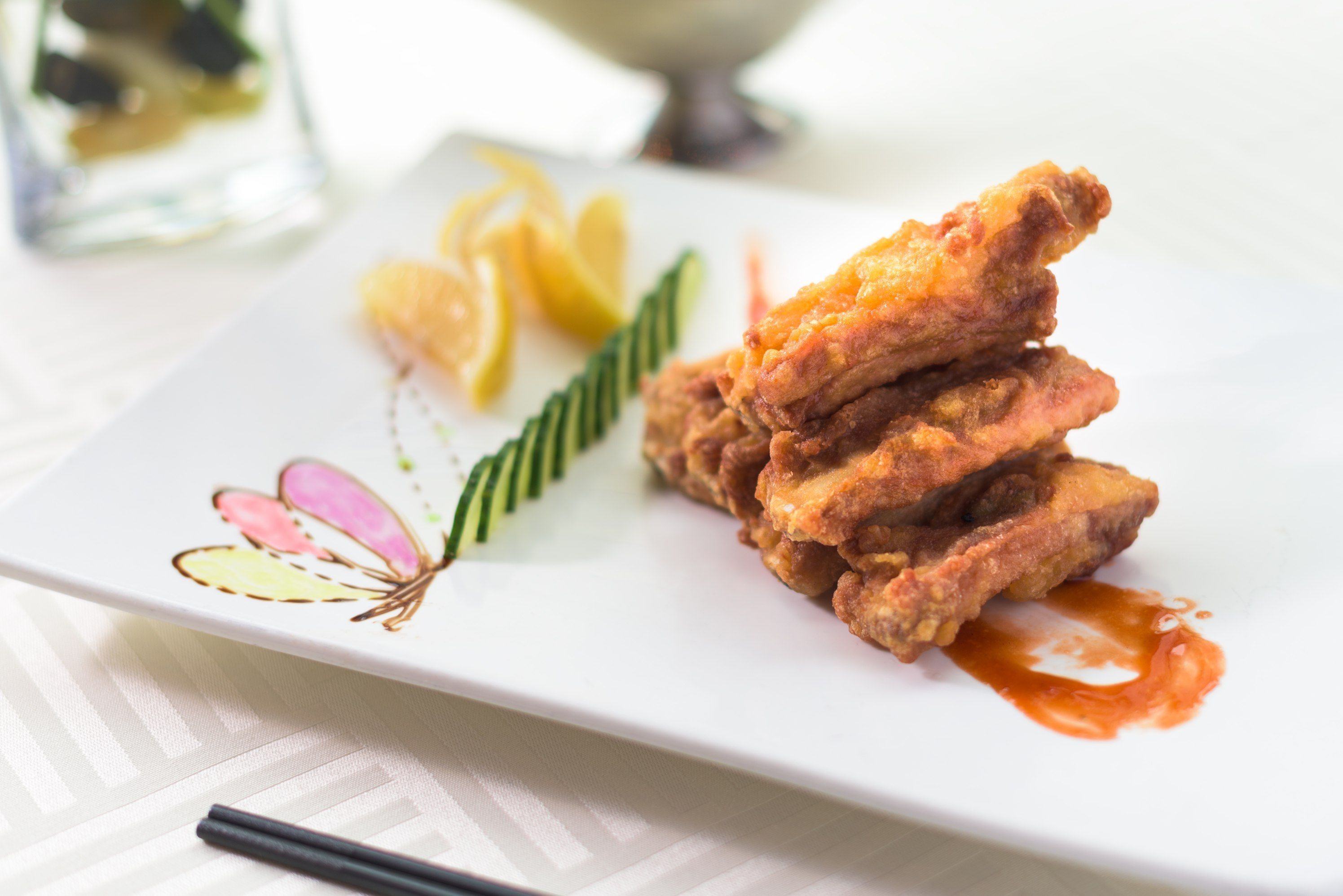 A plate of fried chicken with lemon wedges and a decorative leaf.