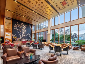 A spacious lobby with leather seating, a large wall mural, and a view of the outdoors through large windows.