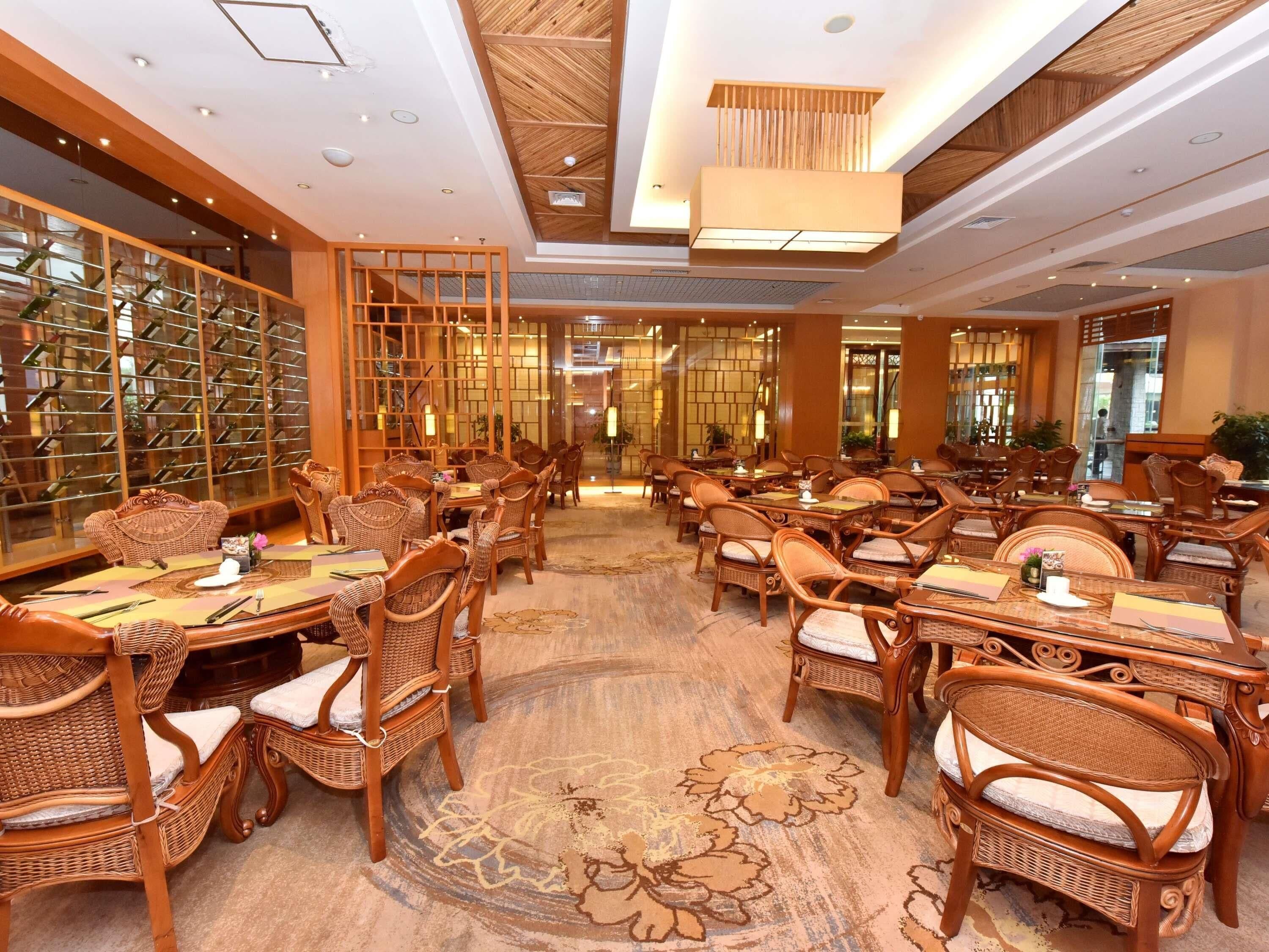 A hotel dining area with multiple tables and wicker chairs, a patterned carpet, and a wine rack in the background.