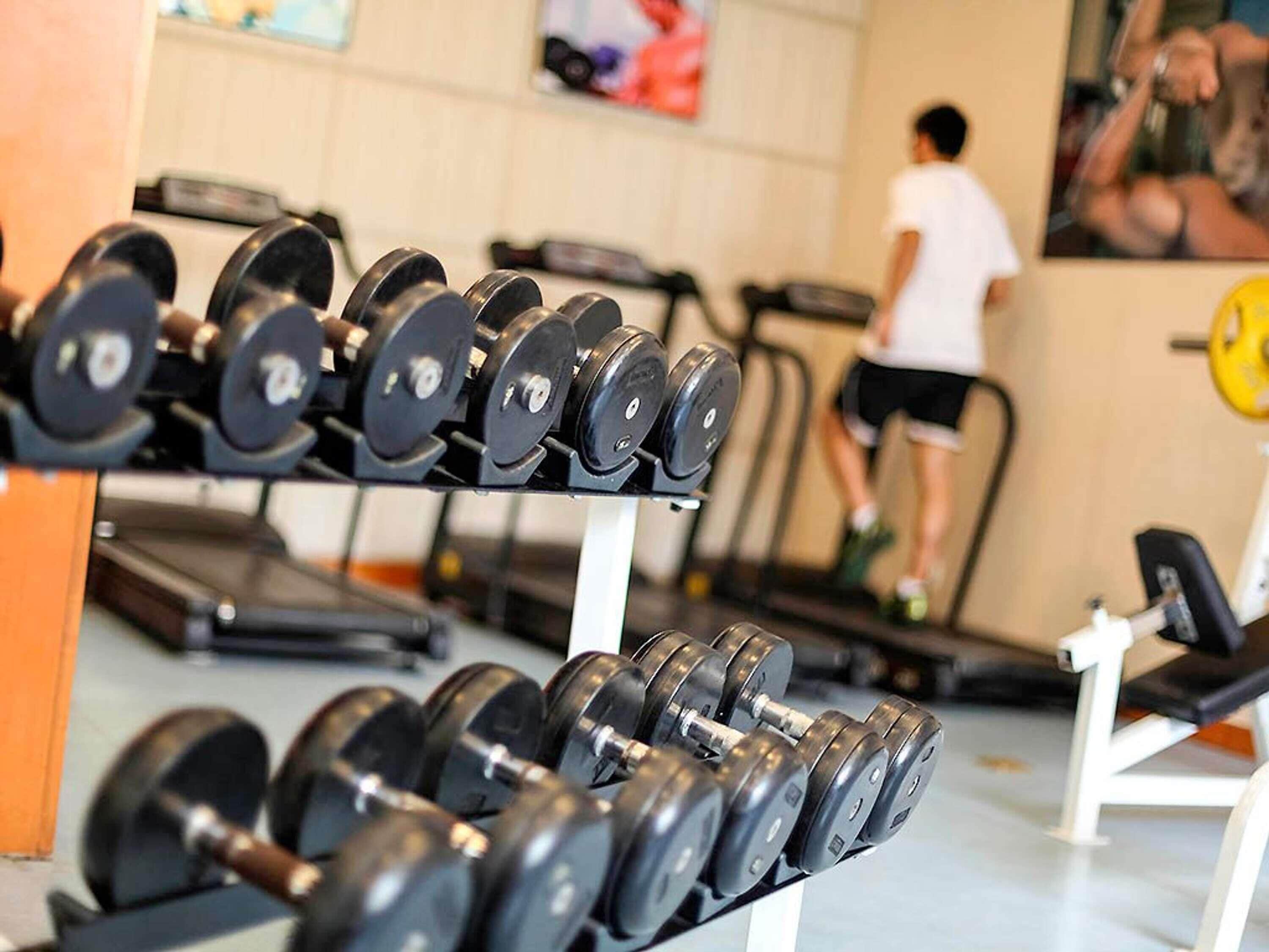 Un gimnasio con filas de mancuernas y una cinta de correr al fondo.