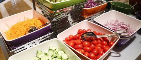 A buffet table with various food items including sliced cucumbers, cherry tomatoes, shredded carrots, and mixed salad.