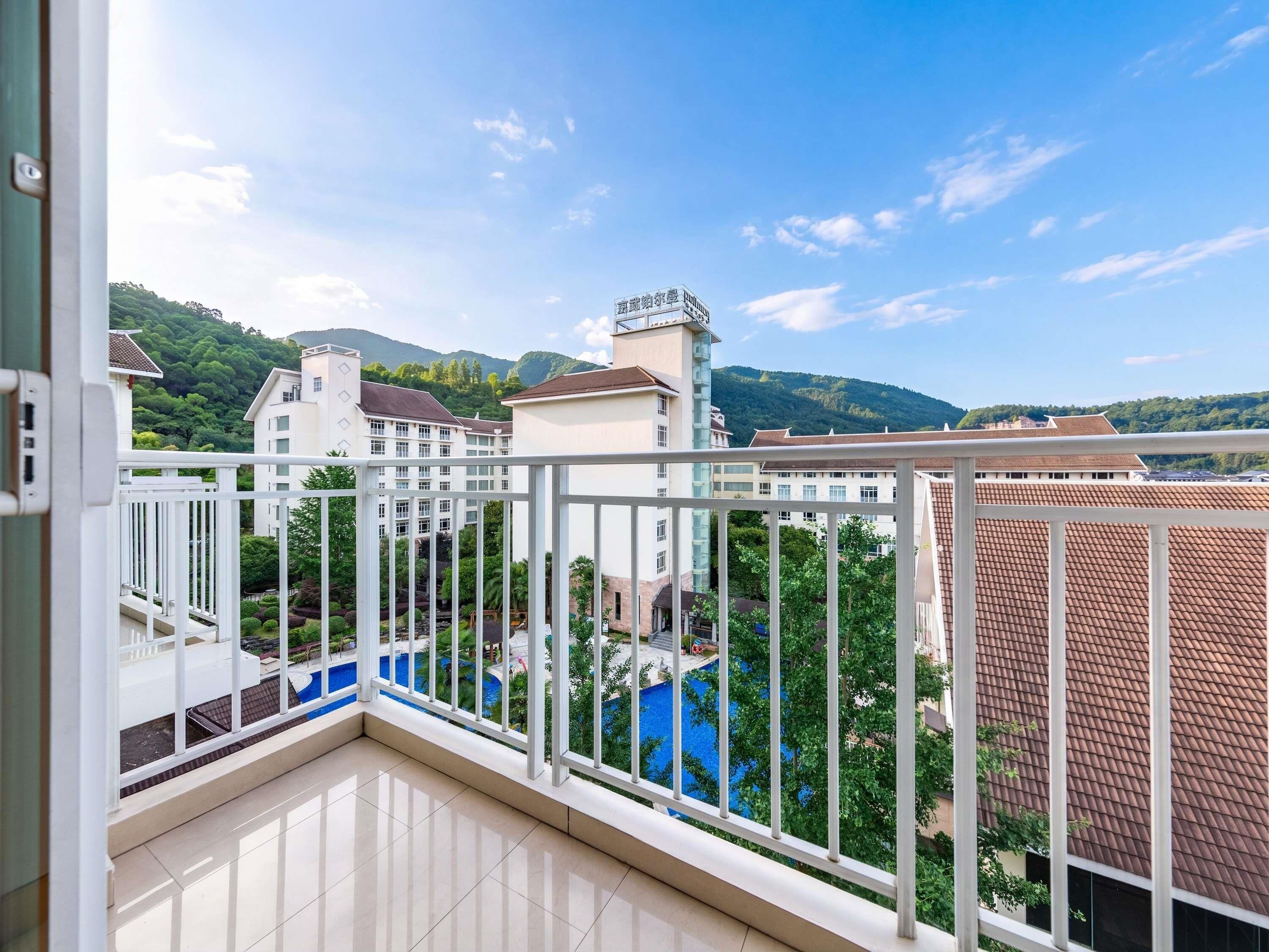 A balcony with a view of a swimming pool, buildings, and a hilly landscape.