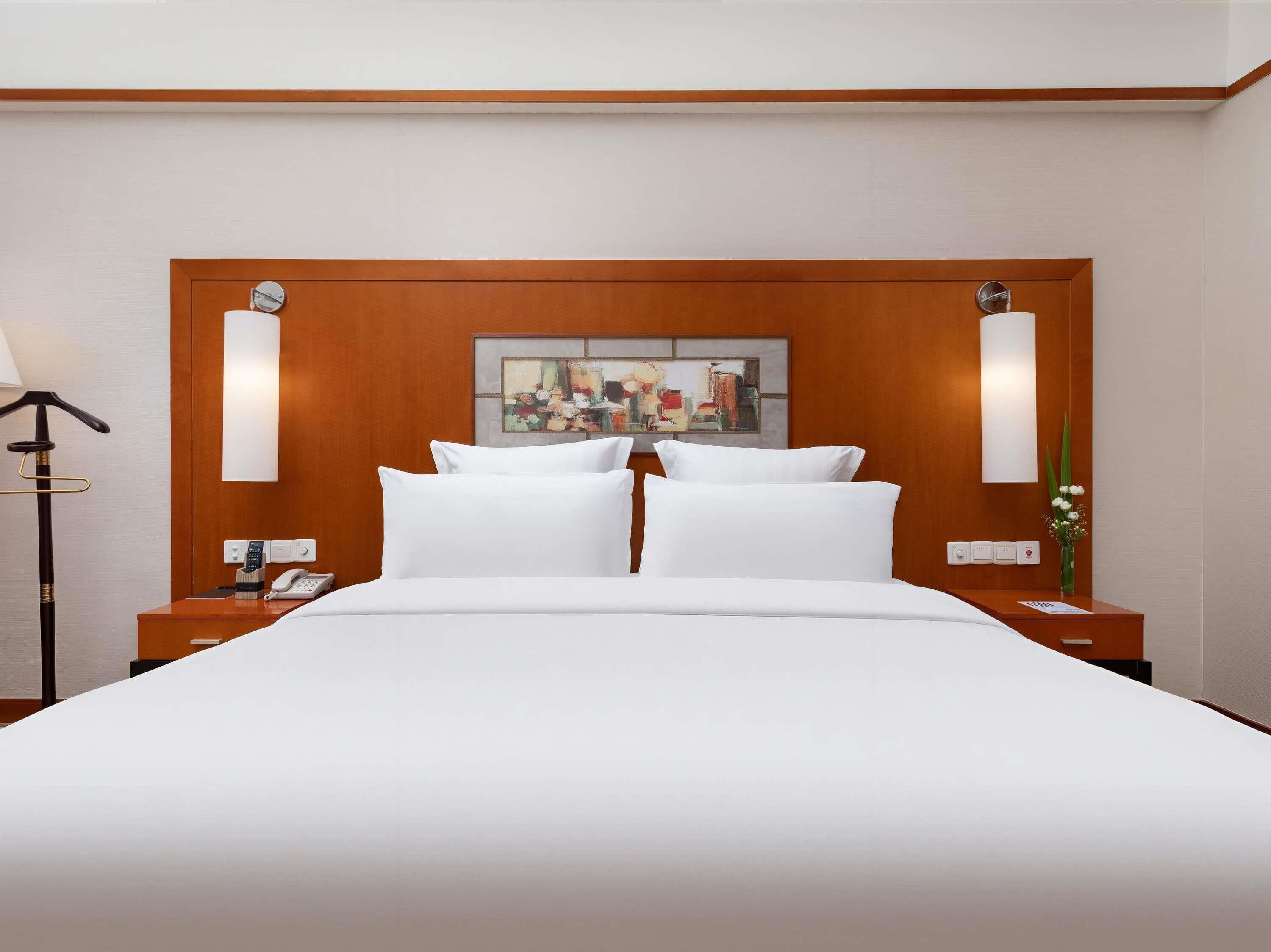 Une chambre d’hôtel avec un grand lit, deux tables de chevet, une lampe, un tableau et un vase rempli de fleurs.