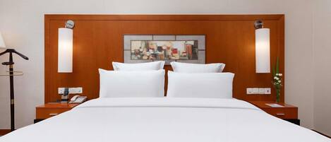 Une chambre d’hôtel avec un grand lit, deux tables de chevet, une lampe, un tableau et un vase rempli de fleurs.