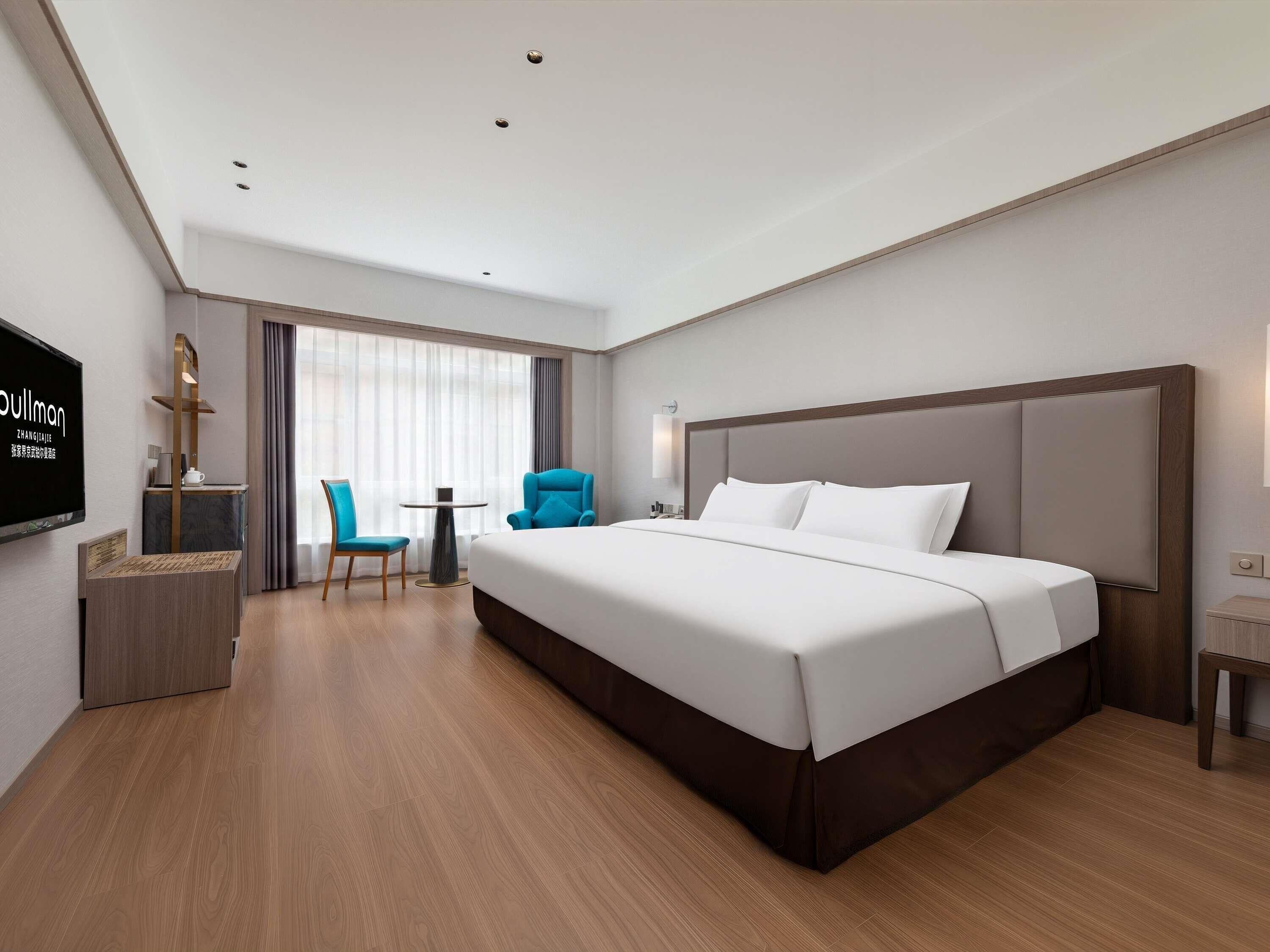 A hotel room with a large bed, a desk with a chair, a television, and a window with curtains.