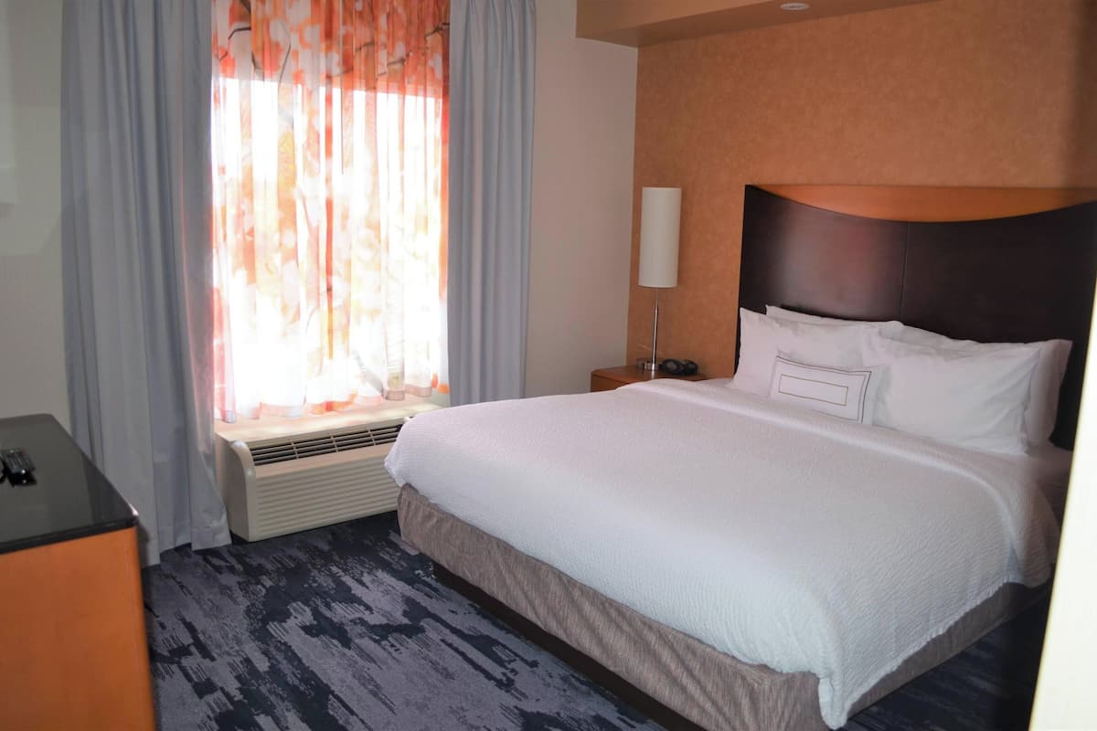 A hotel room with a large bed, a bedside table, a lamp, and a window with curtains.