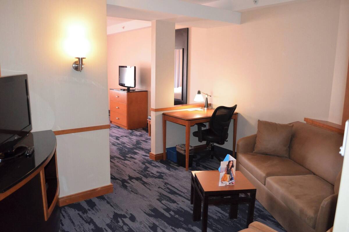 A hotel room with a TV, a desk, a chair, a sofa, and a small table with a magazine.