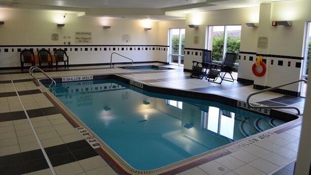 An indoor swimming pool with marked shallow and deep ends, lounge chairs, and a lifeguard station.