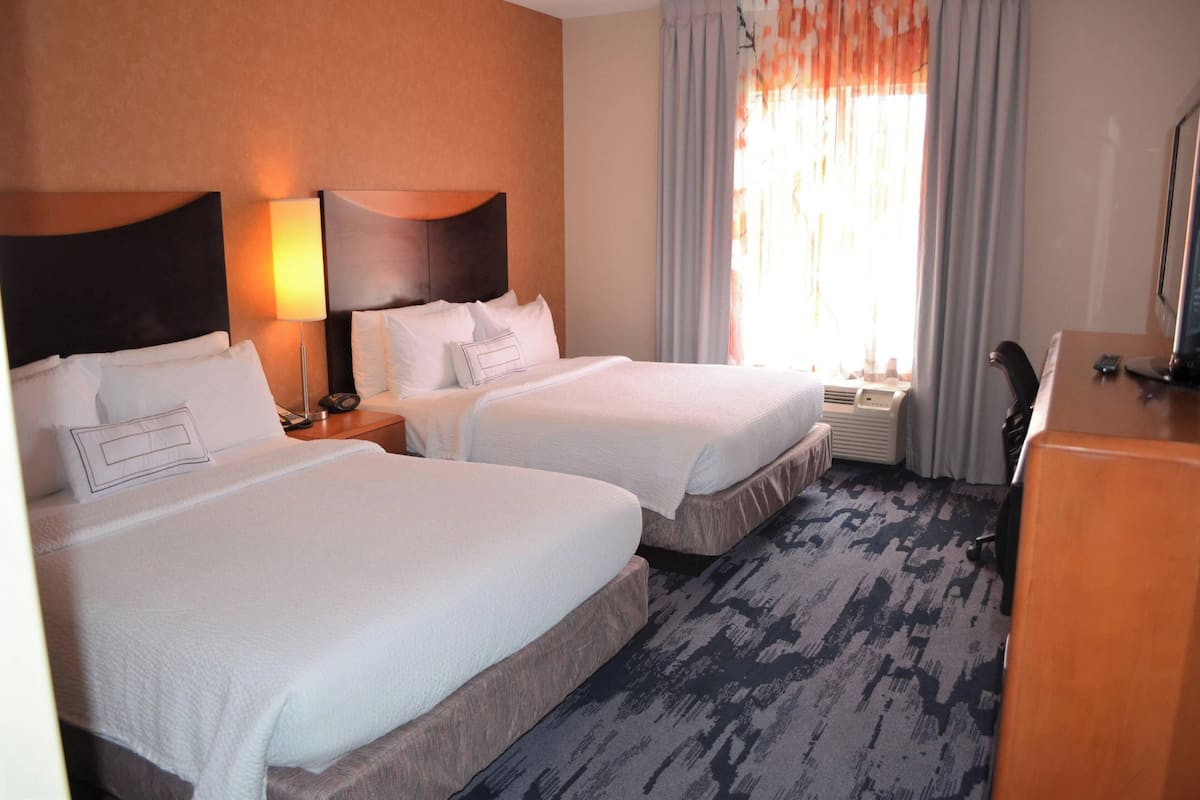 A hotel room with two beds, a desk, a chair, and a window with curtains.