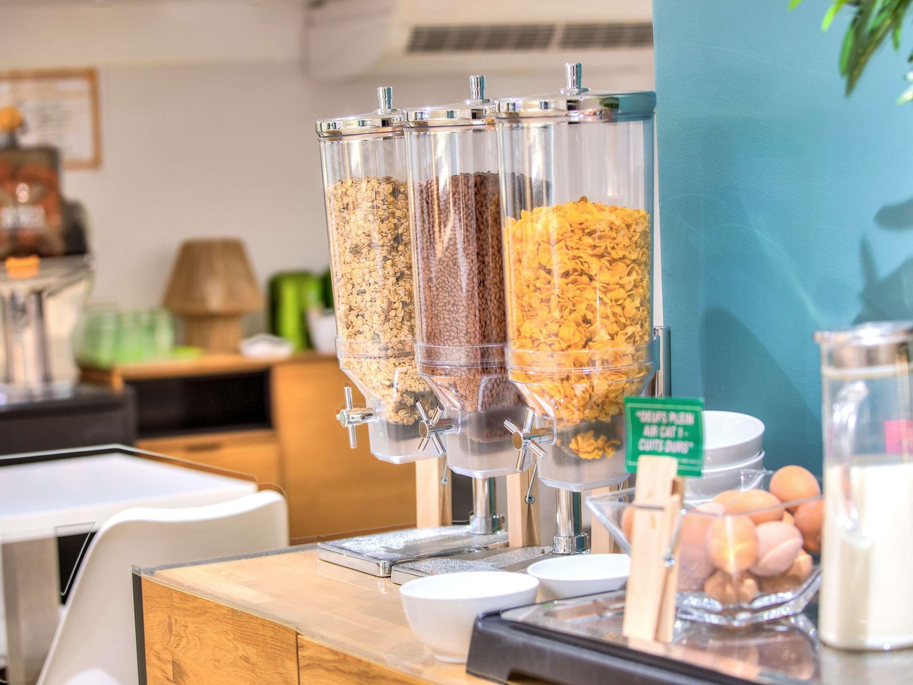 A breakfast bar with three dispensers filled with granola, nuts, and cereal flakes.