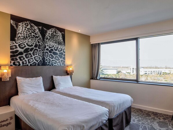 Habitación de hotel con dos camas, un ventanal con vista a la ciudad y una obra de arte con estampado de leopardo en la pared.