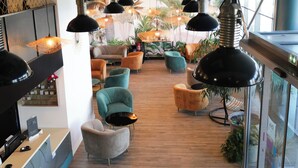 Un intérieur moderne avec plusieurs coins salon, des luminaires suspendus et une vue sur les palmiers à travers de grandes fenêtres.