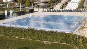 Un espace piscine doté d’un toboggan, entouré de verdure et bordé d’une colline.