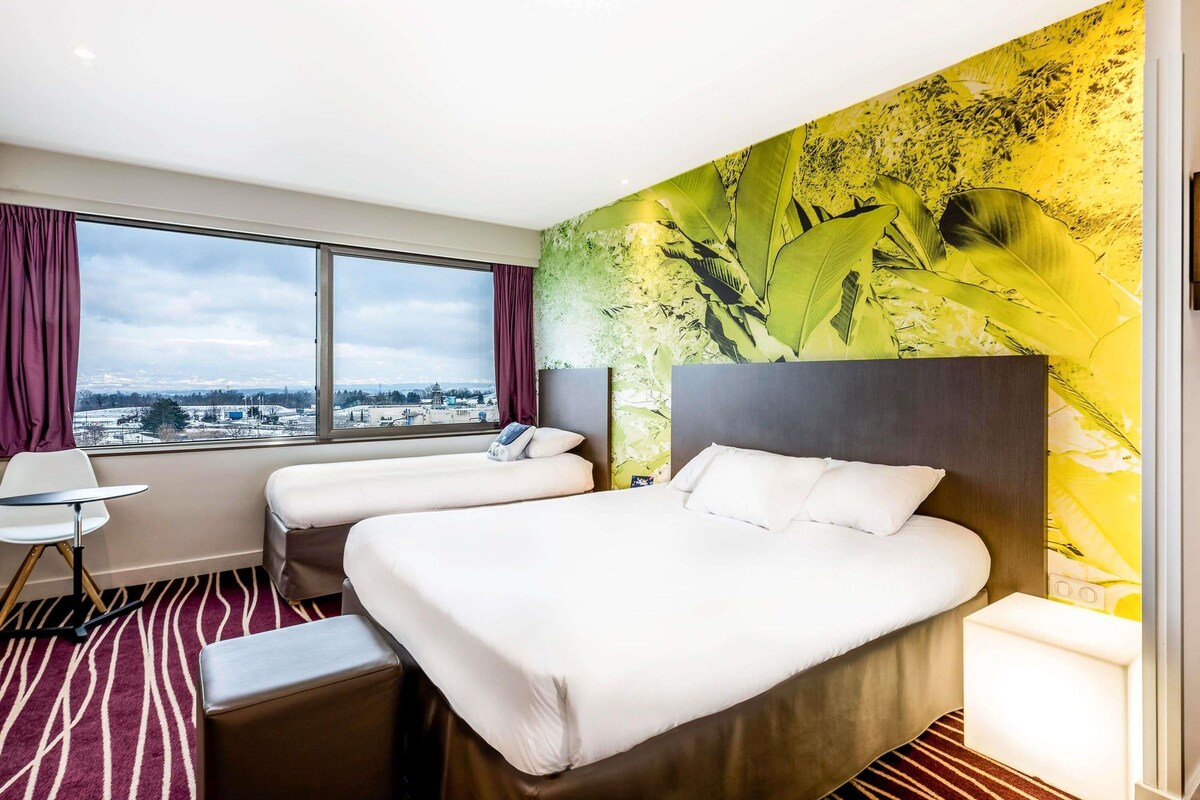 Une chambre d’hôtel avec deux lits, un bureau, une chaise et une grande fenêtre donnant sur la ville.