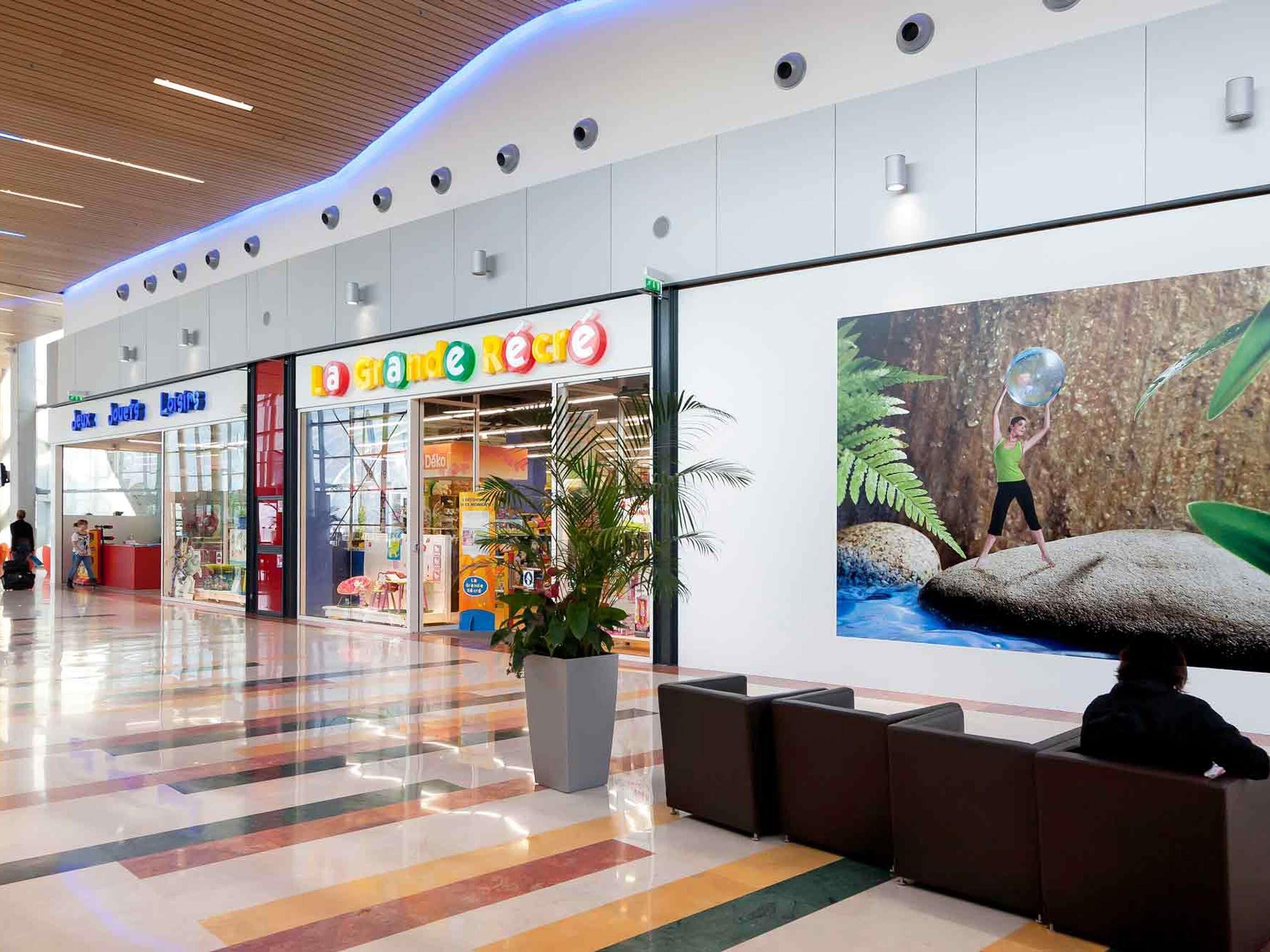 A shopping mall corridor with stores, a large potted plant, and a mural of a person with a ball.