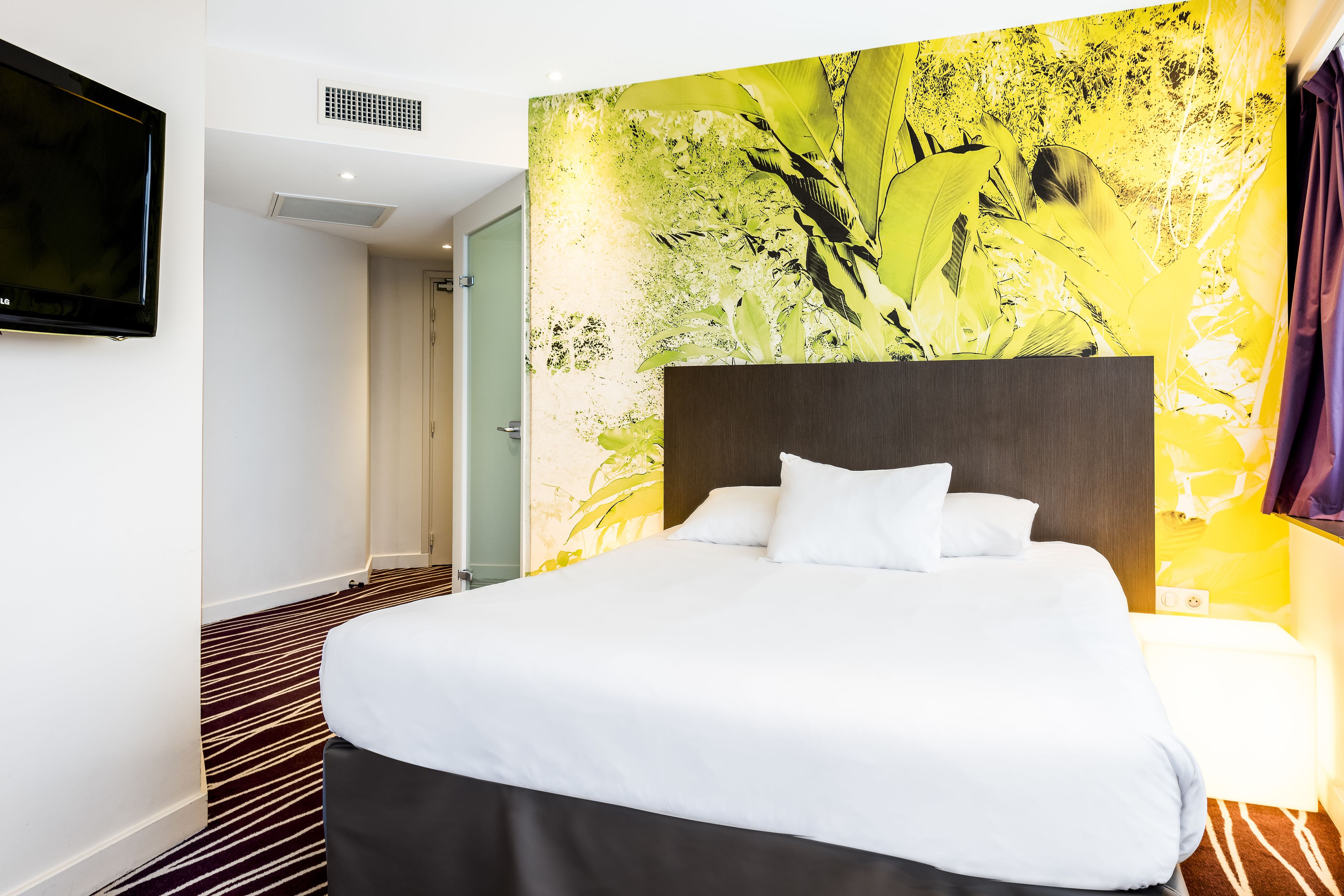 Habitación de hotel con una cama grande, un televisor de pantalla plana en la pared y un mural colorido.
