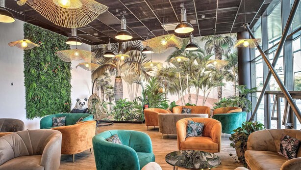 Un intérieur moderne doté de plusieurs espaces de détente, d’un mur végétal et d’un plafond agrémenté de luminaires originaux.