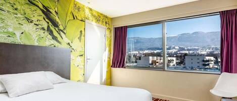 Habitación de hotel con una cama, ventana y vista a la ciudad, además de un mural tropical en la pared.